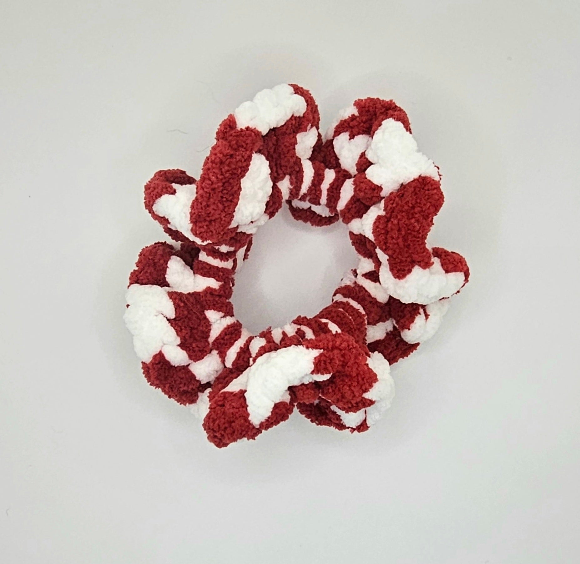 Plushie white and red yarn crochet around a hair elastic to create a ruffly scrunchie. The yarn creates a checker pattern.