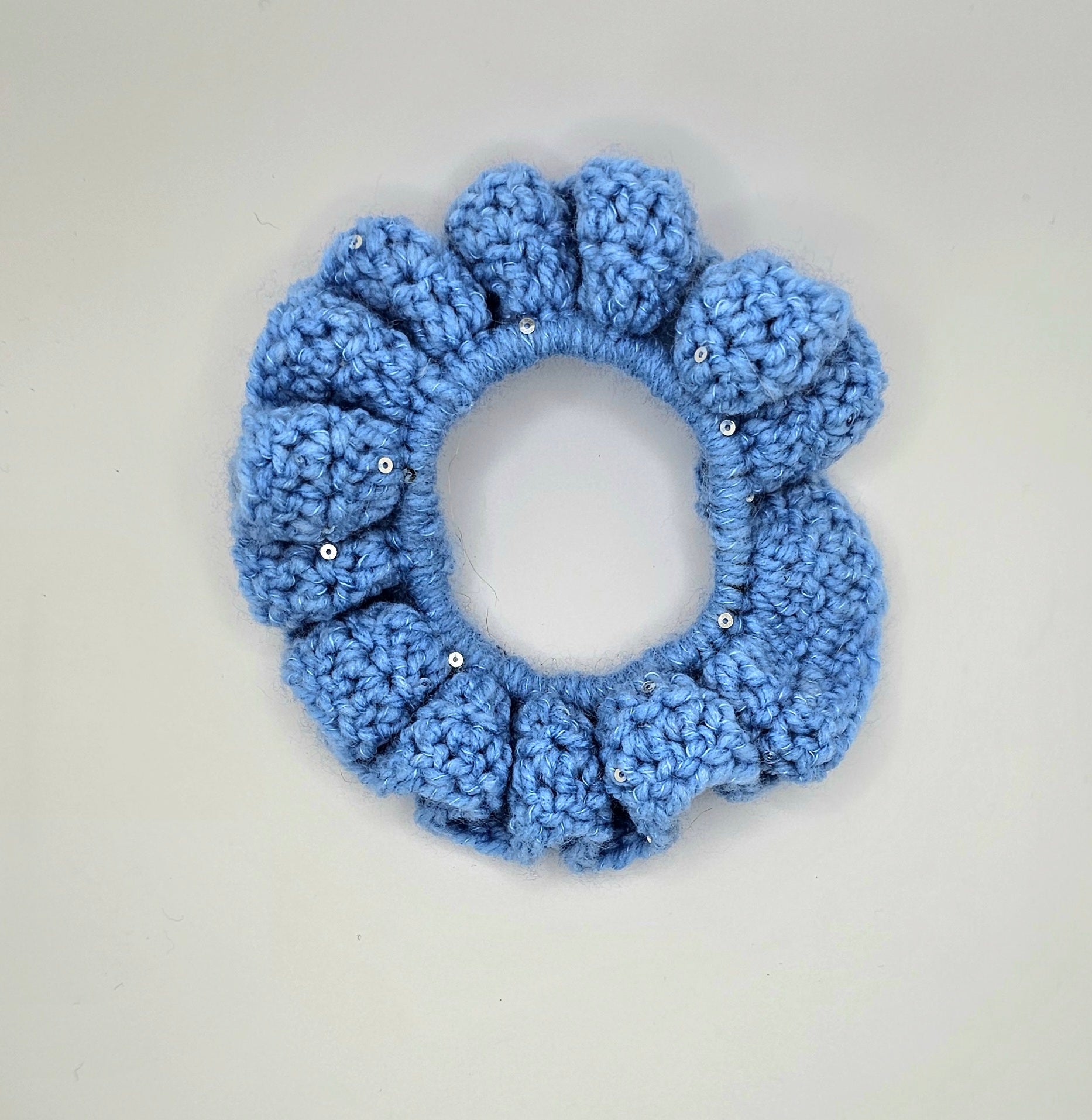 Worsted blue yarn with sequin crochet around a hair elastic to create a ruffly and sparkly scrunchie.