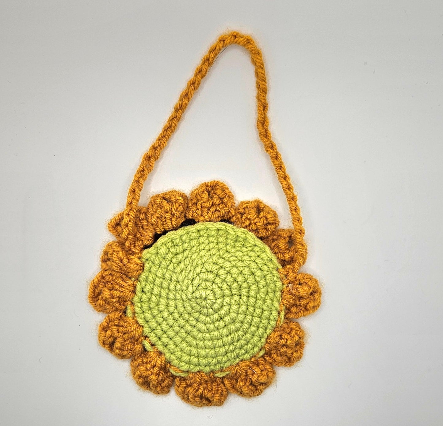 Crochet sunflower pouch. Back side. The center of the flower is made from light green yarn that spirals as it goes out. The petals are made from a marigold-yellow colored yarn--as well as the pouches handle.