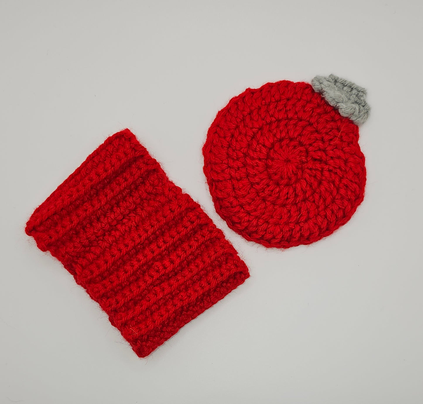 Red coffee cozy and red Christmas tree ornament themed red coaster laying flat on a white surface to highlight detail.