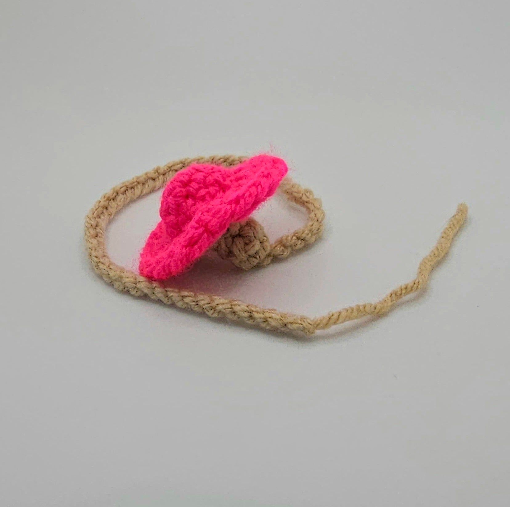 Neon Pink yarn mushroom cap with a beige stem that turns into a crochet braid.