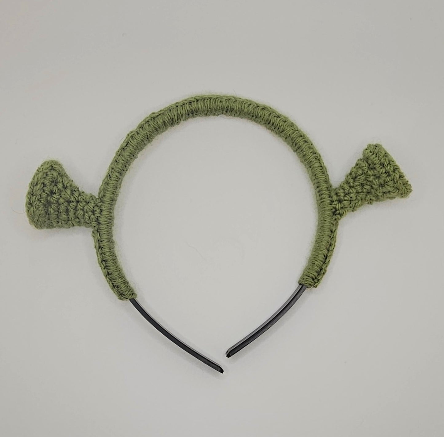 Olive green yarn over black plastic headband. The headband has crochet Shrek ears attached to the headband.
