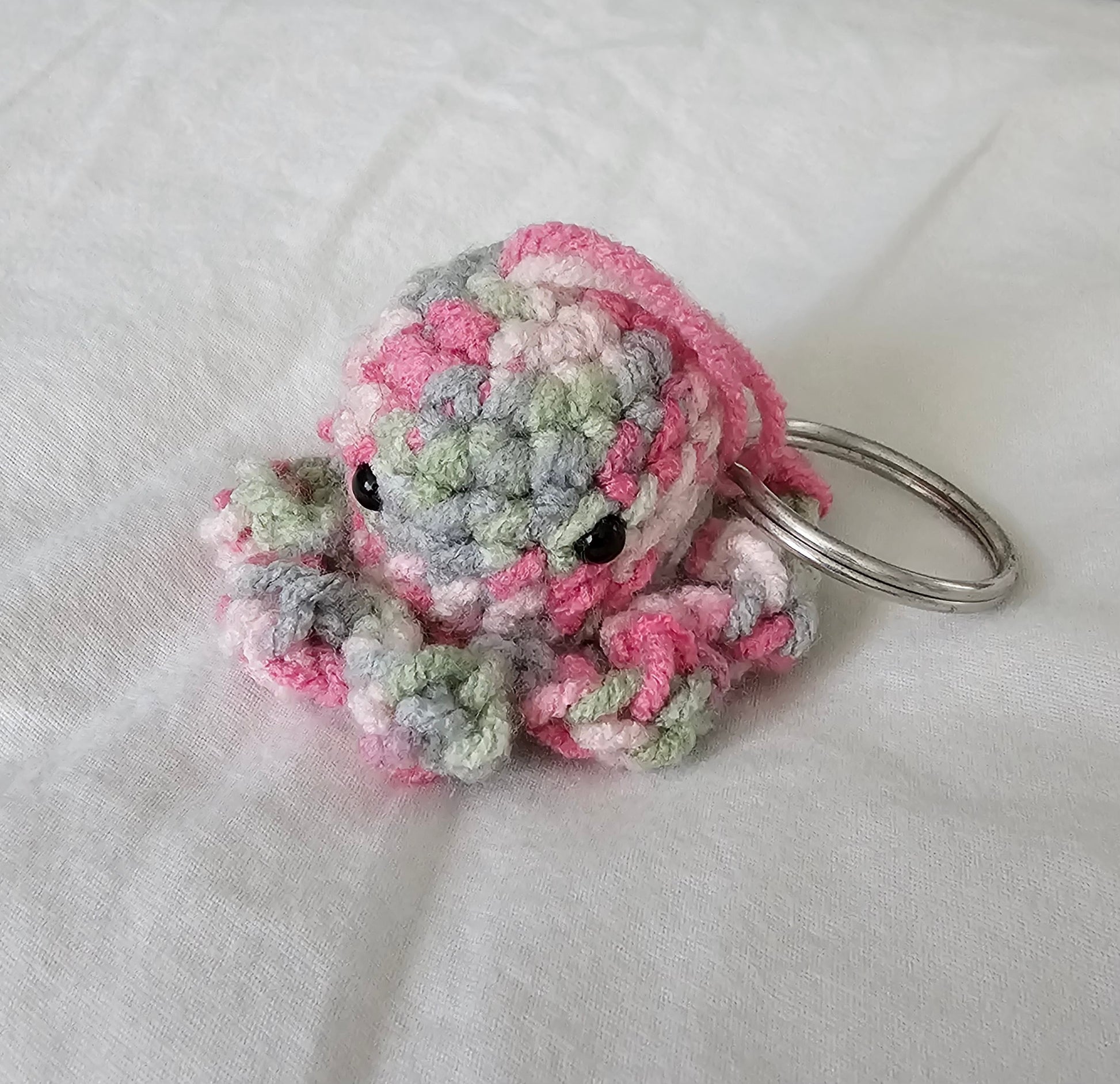 Small octopus keychain made from a multi color yarn which has a mix of soft pink, cream and mint colors. The octopus also has small black eyes and the key ring is attached through the top of the head by the same yarn the octopus is made out of.