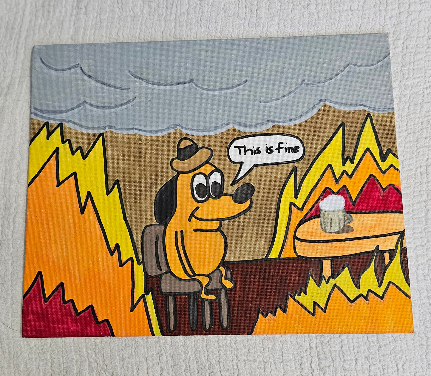 Canvas painting with a dog sitting on a chair wearing a fancy hat and smiling. He is surrounded by fire in a room with a table with a table he can't reach. On the side of his face there is a text bubble that says "This is fine". There are clouds of smoke covering the ceiling.