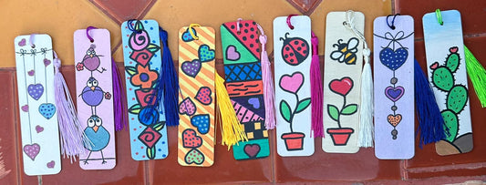 Assortment of wooden bookmarks with different designs painted on them and colorful tassels.
