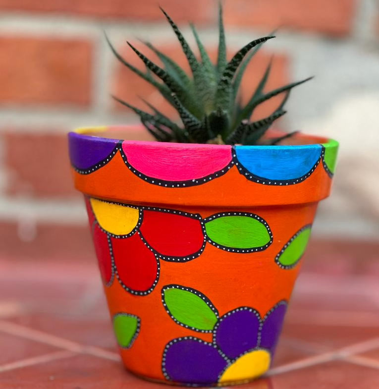 Decorative pot with painted on flower designs. The flowers are red and purple wit a bright yellow center and bright green leaves. these flowers are outlined in black the outline is dotted all along with white dots. The flowers lie on top of a bright orange background.
