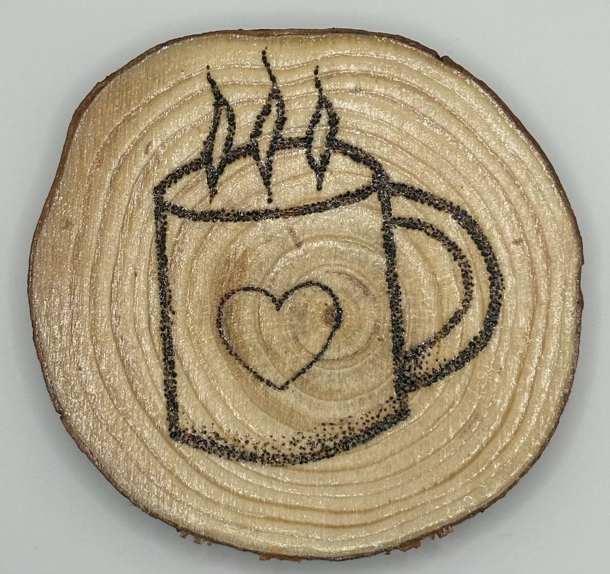 Wooden disk with a design of a coffee cup with a heart on it and some steam leaving the cup burned onto it.