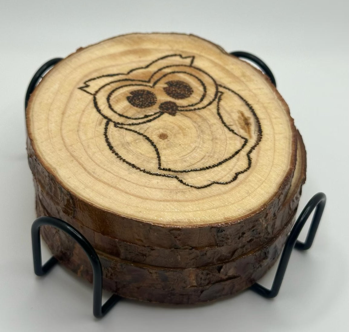 4 wooden disks stacked on top of each other. these disks sit inside a metal stand that encases them. The disk on top has a design of a cute, big eyed owl burned onto it.