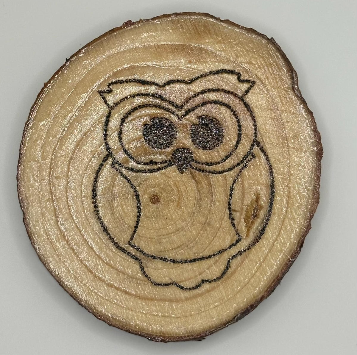 Wooden disk with a burnt on design. The design is a cute, big eyed owl.