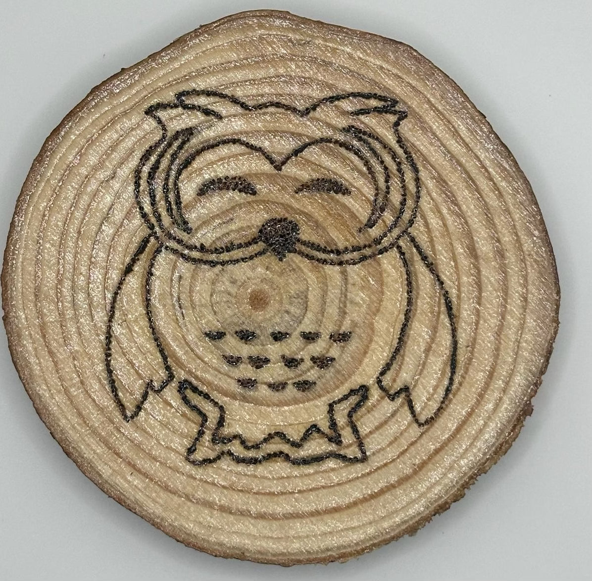 Wooden disk with a burnt on design. The design is a cute owl that is smiling by closing both eyes..