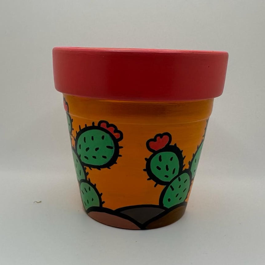 Decorative pot with an orange-yellow base, there are prickly pear cacti with red flowers growing out of mounds of dirt.. The ridge of the pot is painted orange-red.