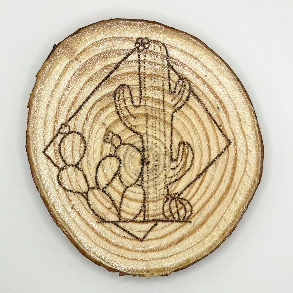 Wooden disk with a design burned onto it, the design cacti which are partially encased in a square.