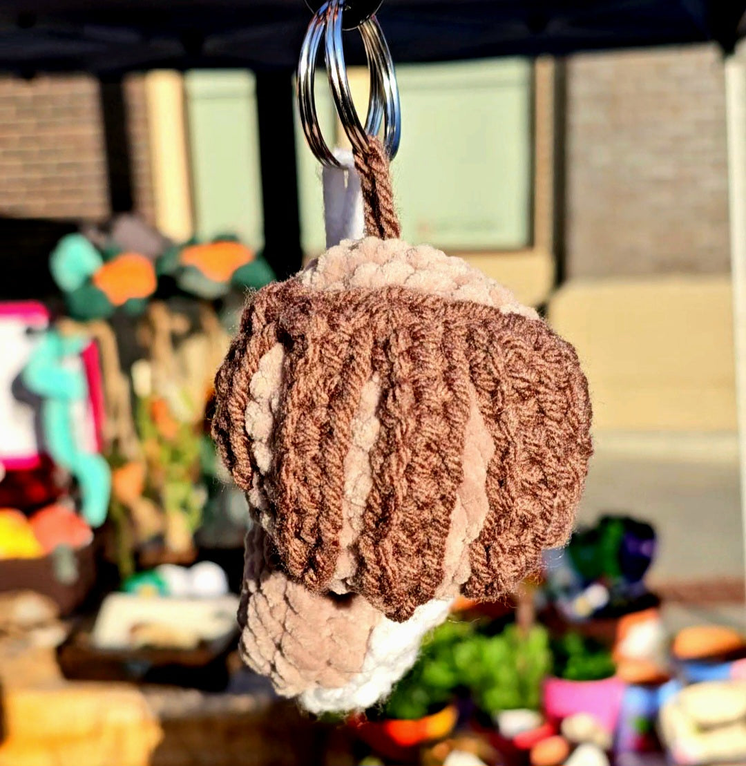 Mexican sweet bread shaped keychain made from beige plush yarn as the bread and the sugar frosting is made from brown thin yarn. The keyring is attached to the sweet bread by yarn the same color as the sugar frosting.